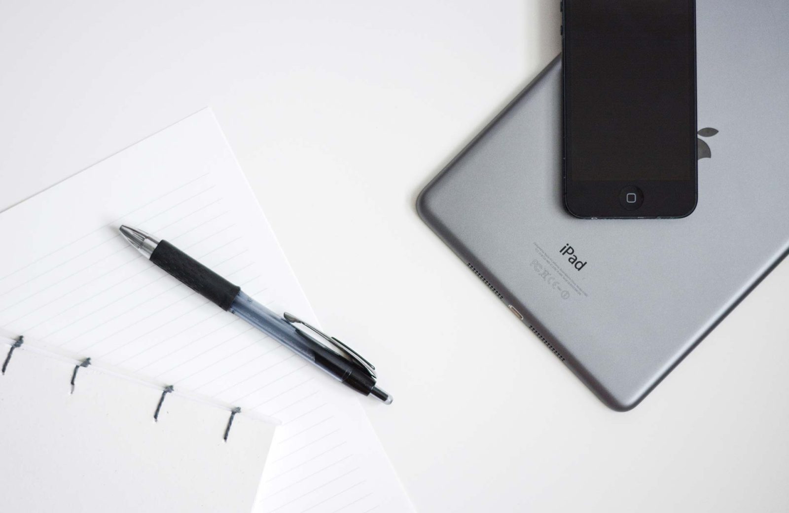 Pen, notebook, iPad, iPhone on white desk
