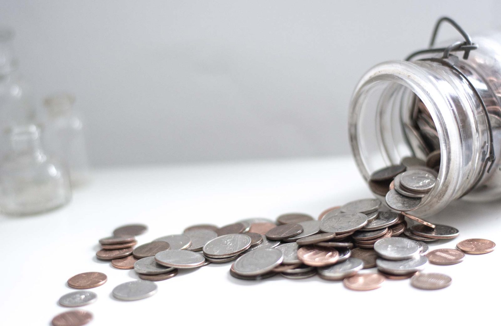 Glass jar spilling coins on white surface